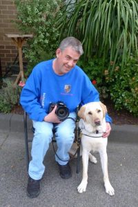 A man holding a camera and posing with his guide dog